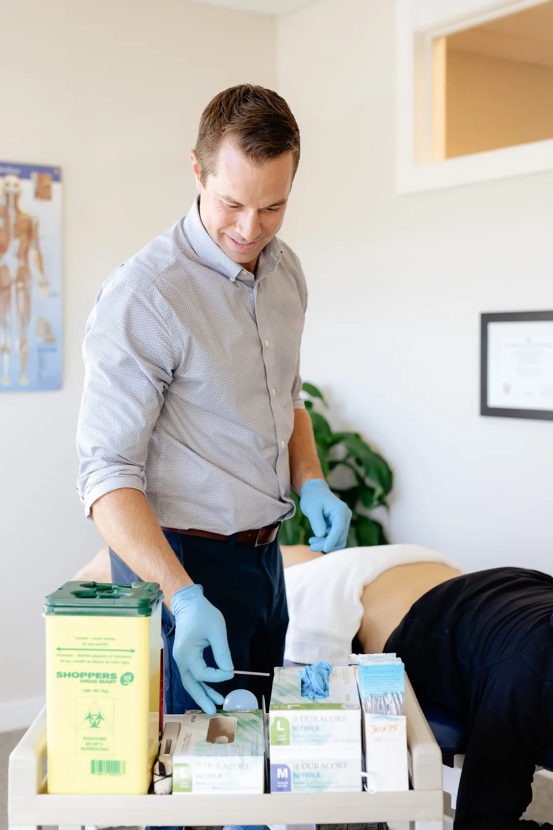 Healthcare professional wearing gloves prepares a medical swab next to a patient on a treatment table.