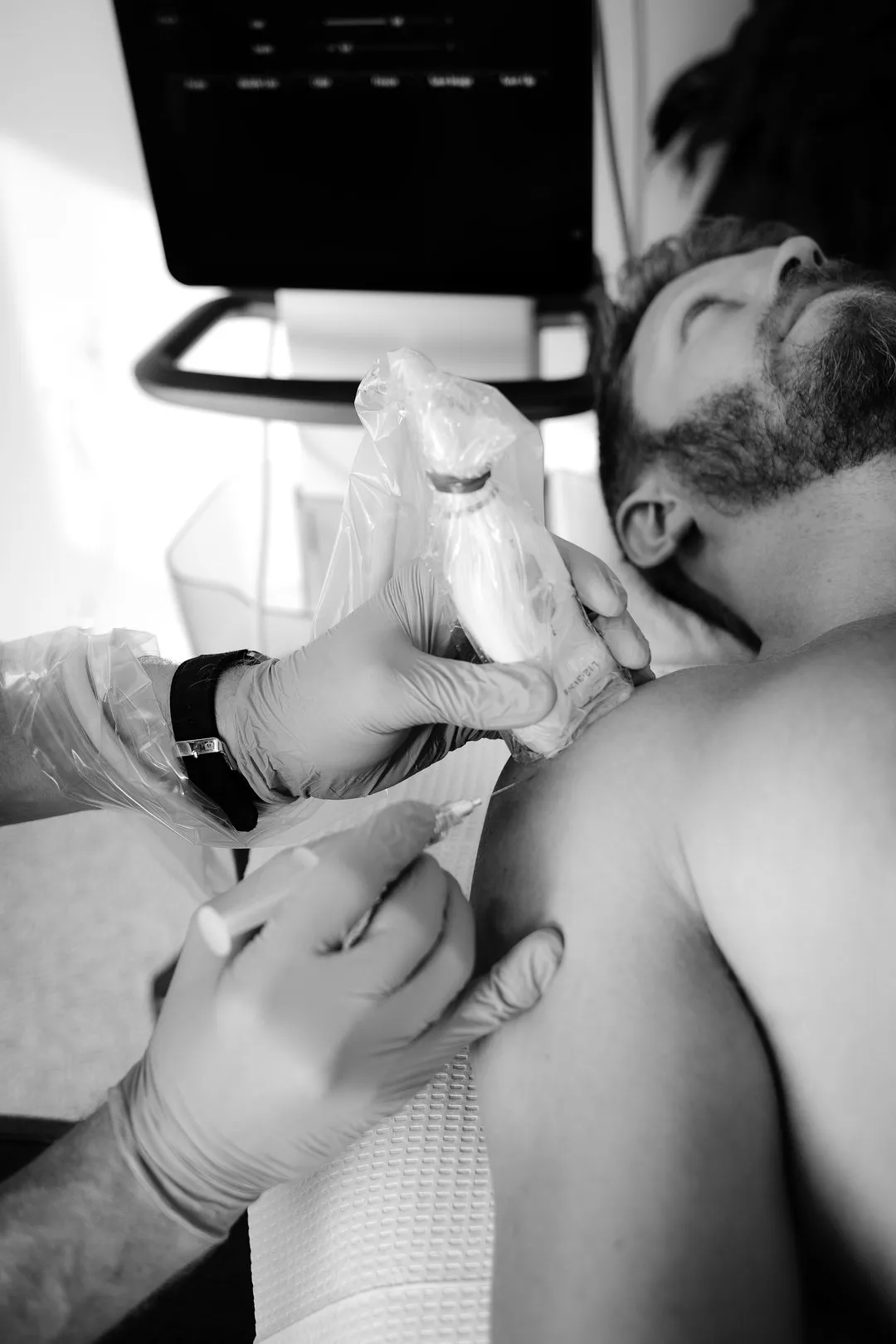 Medical professional wearing gloves injects a patient's shoulder with a syringe during treatment.