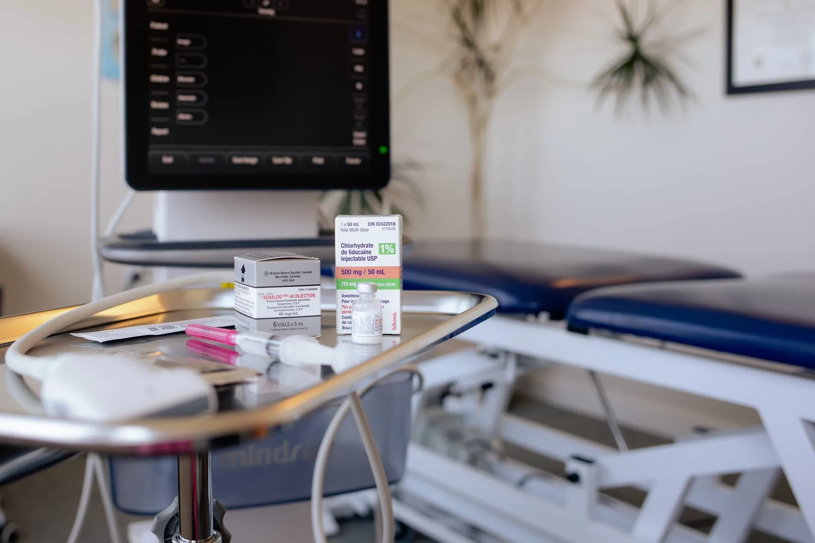 Medical tray with injectable medication boxes, syringes, and a stethoscope in a clinical room.