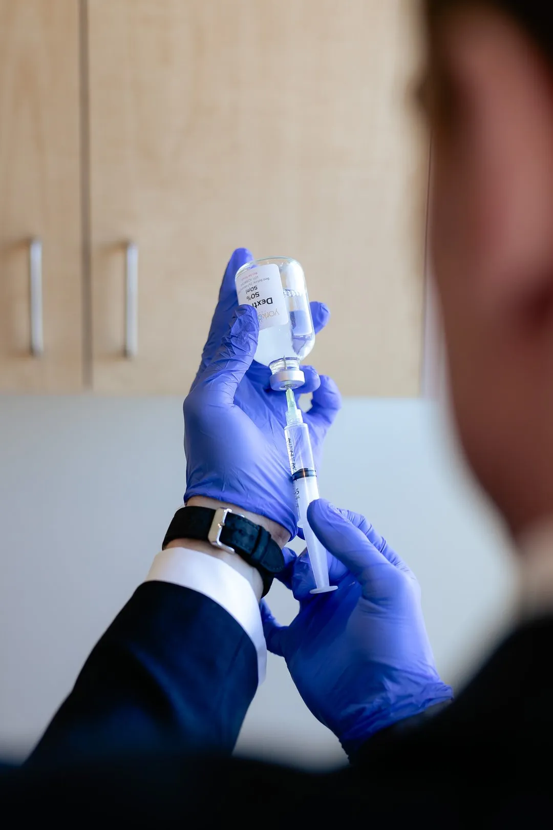 Medical professional wearing blue gloves fills syringe with clear liquid from a vial labeled 50% dextrose.