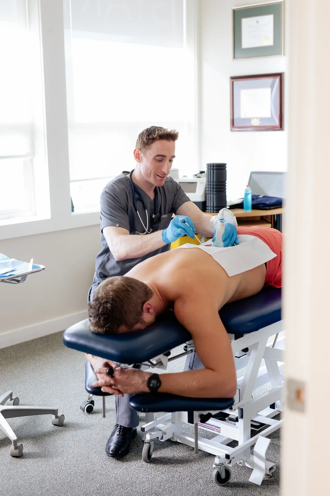Medical professional applying treatment to a shirtless man lying face down on a therapy table.