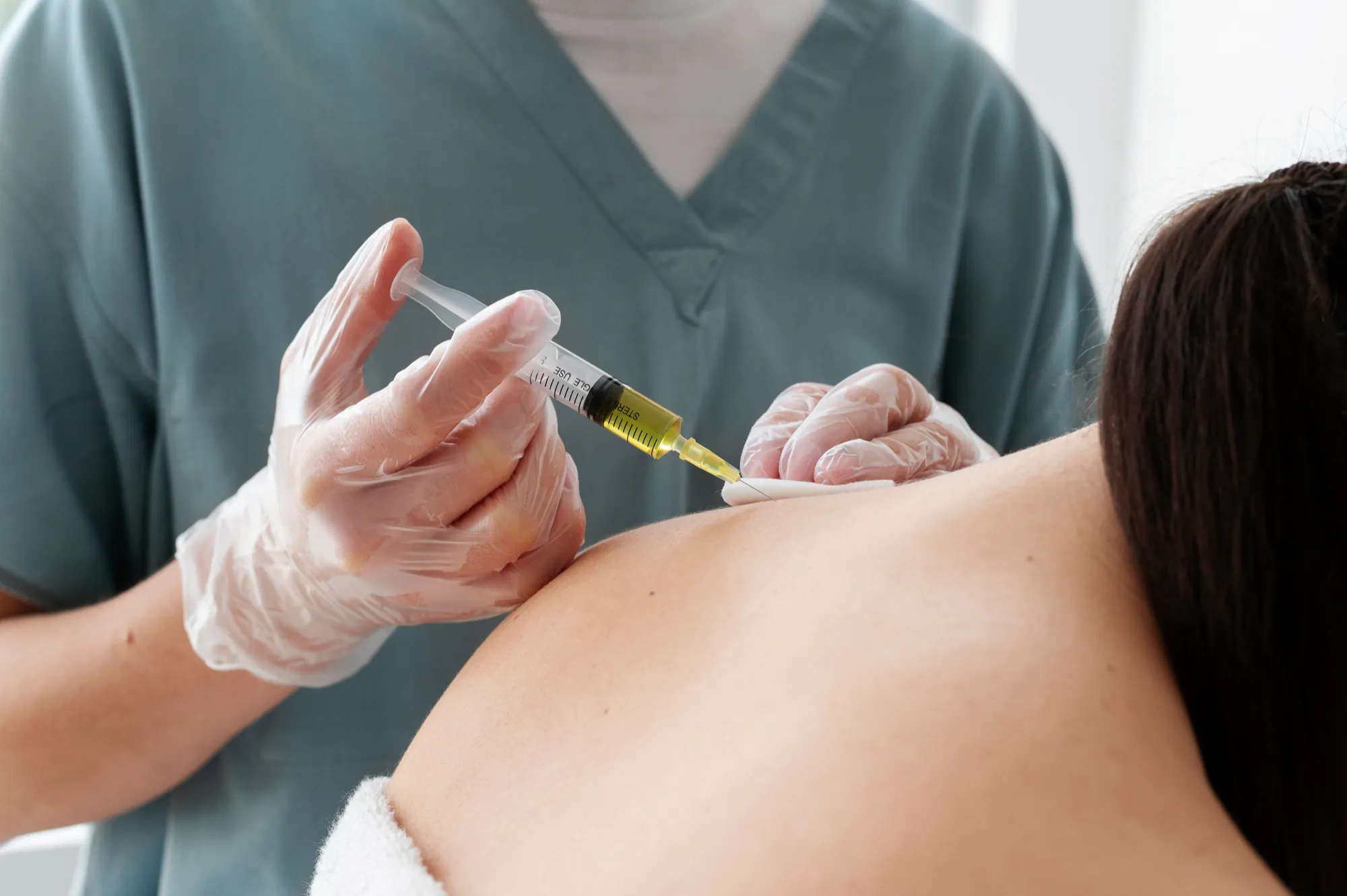 Healthcare worker wearing gloves injecting vaccine or medication into a person's upper arm.