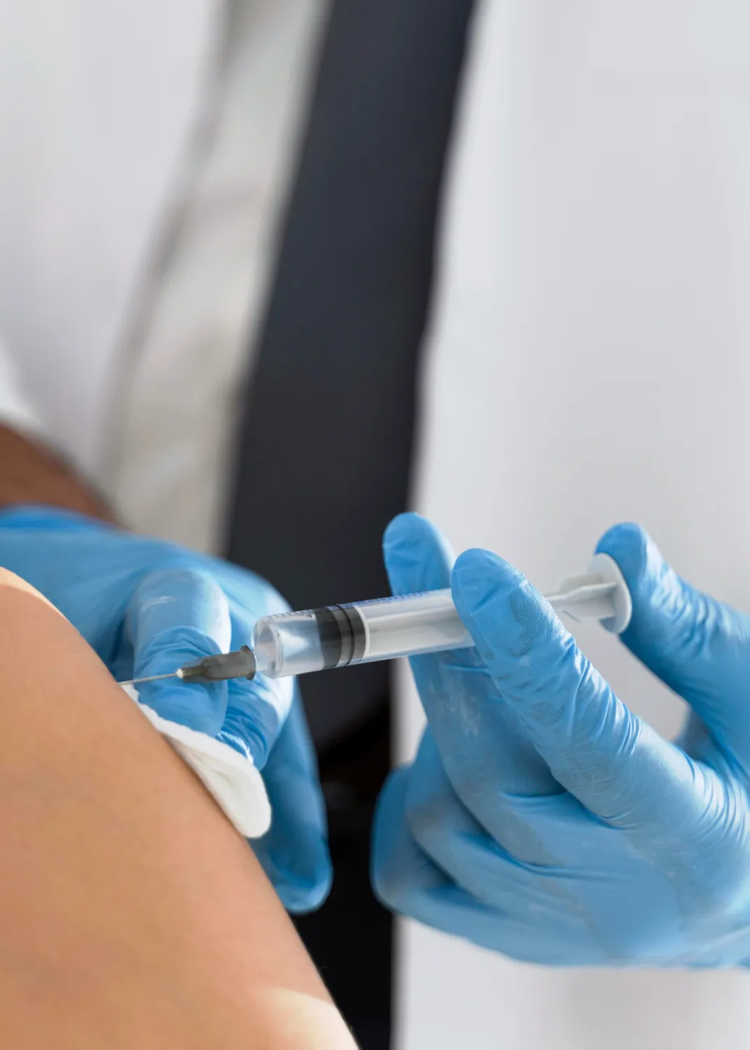 Medical professional wearing blue gloves administering an injection with a syringe to a patient's arm.