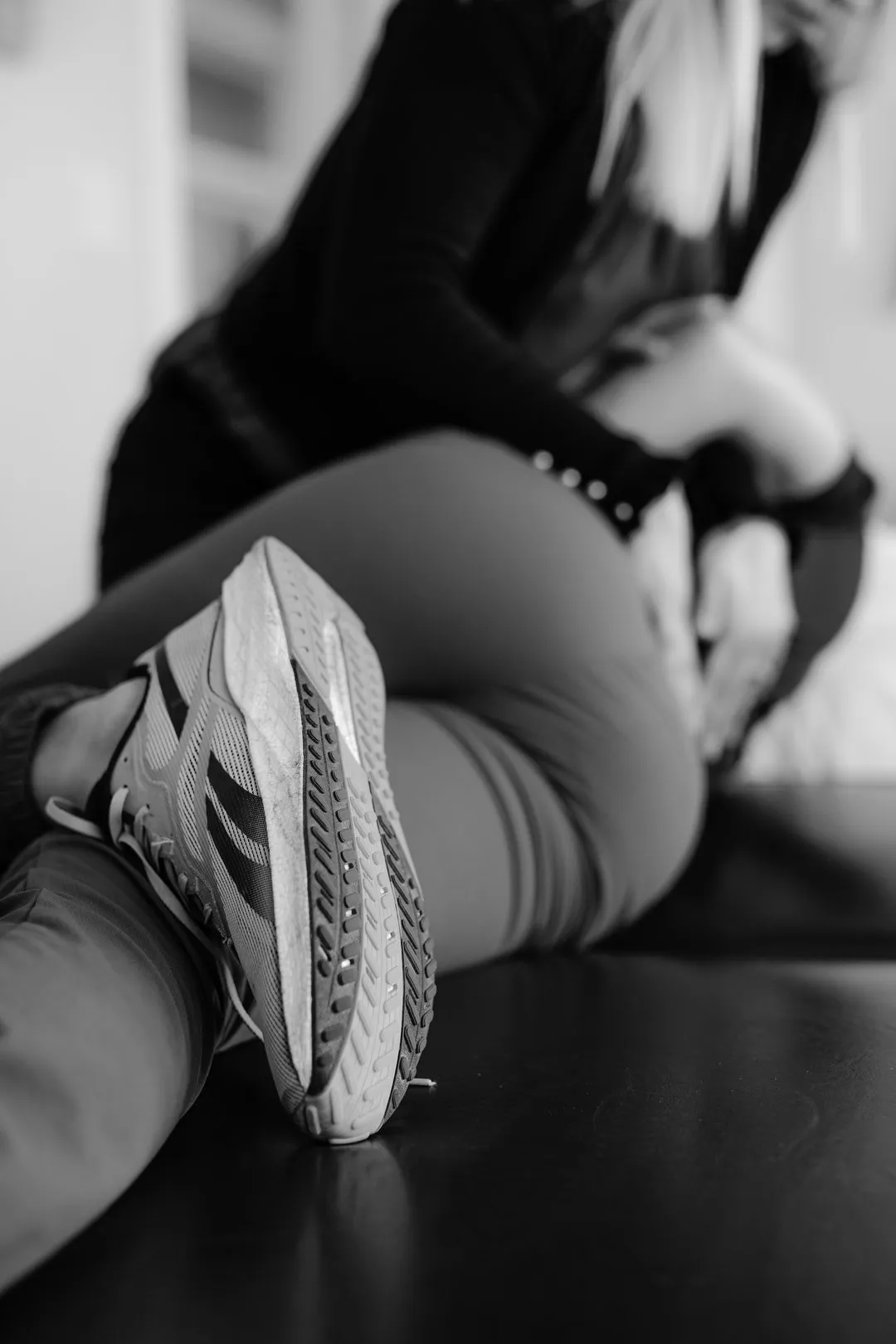 Person in athletic shoes and leggings stretching on floor with assistance in black and white.