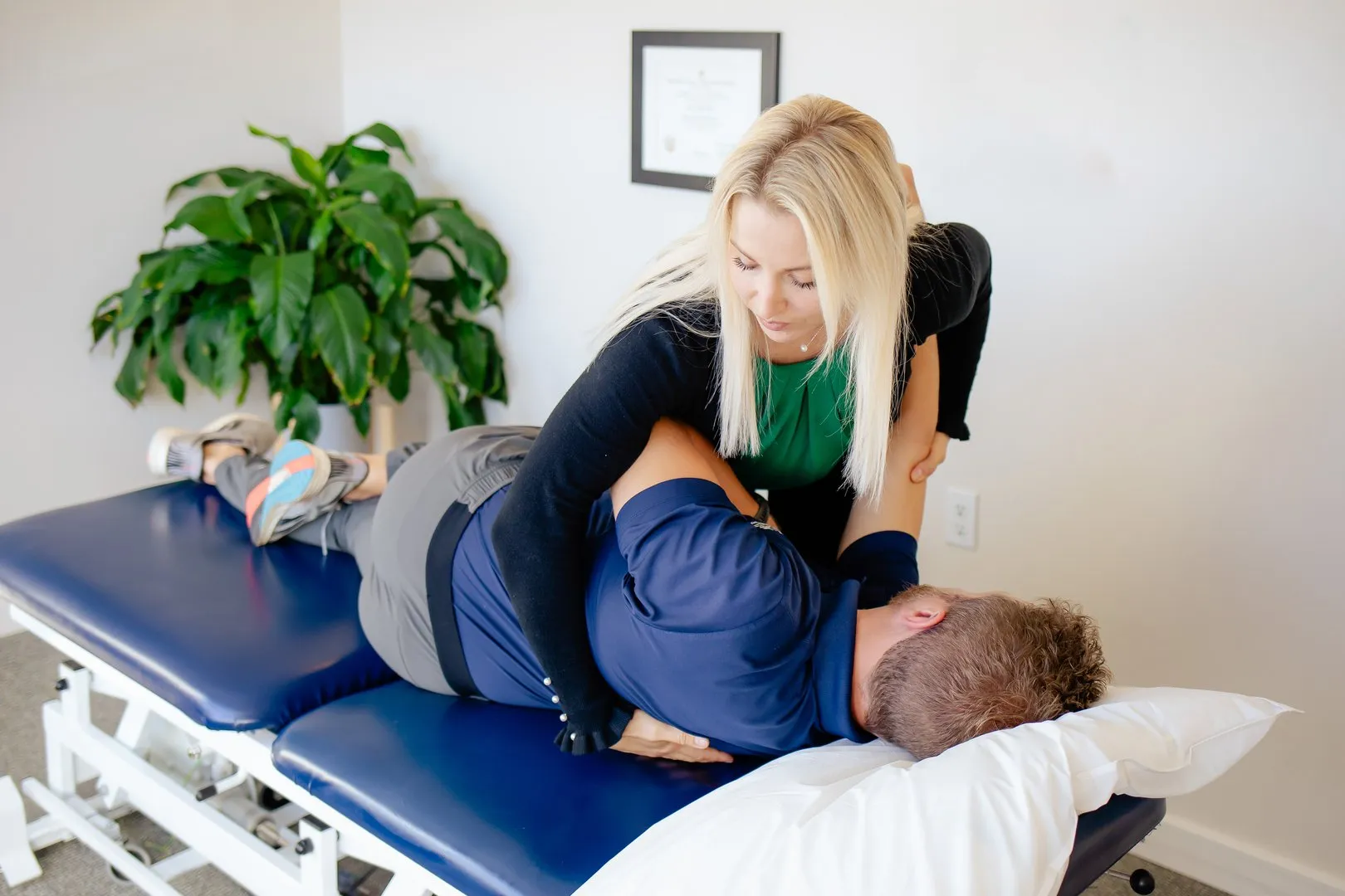 Physical therapist with blonde hair stretching male patient lying on his side on a treatment table.