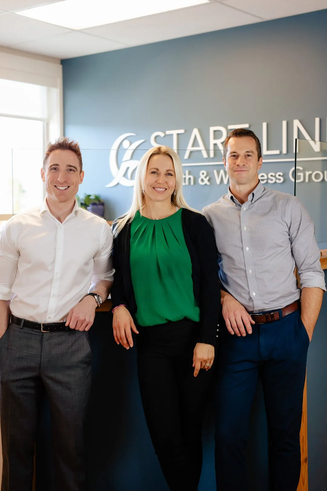 Three smiling professionals standing in front of a START LINE Health & Wellness Group sign.