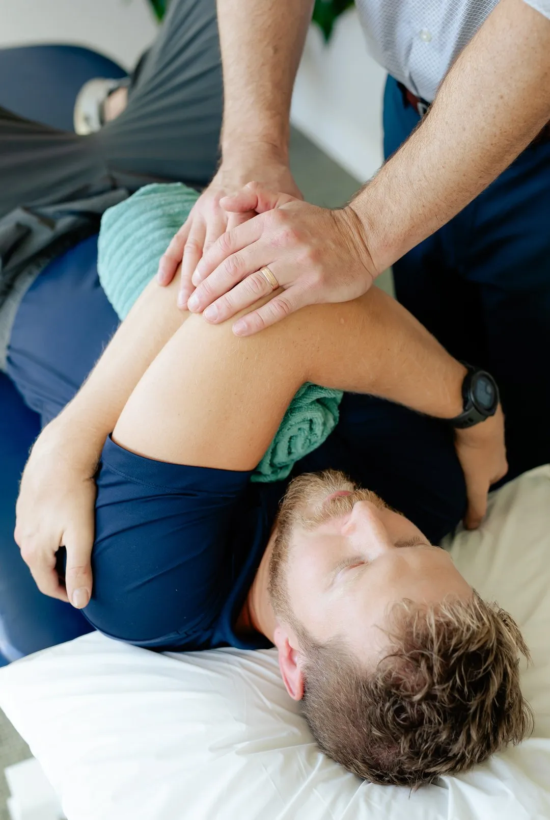 Physical therapist applying pressure to a man's shoulder while he lies on a treatment table.
