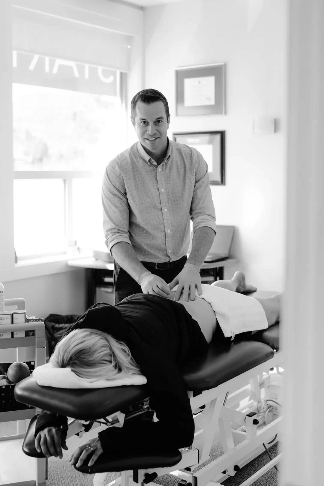 Therapist wearing gloves treats a patient lying face down on a treatment table in a clinic.