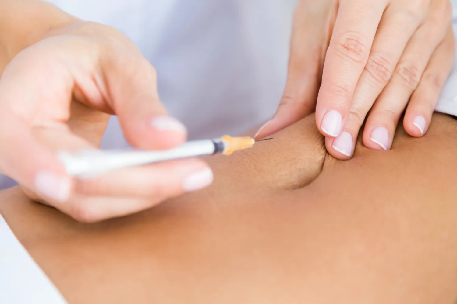 Close-up of a hand holding a syringe about to inject into a person's skin.