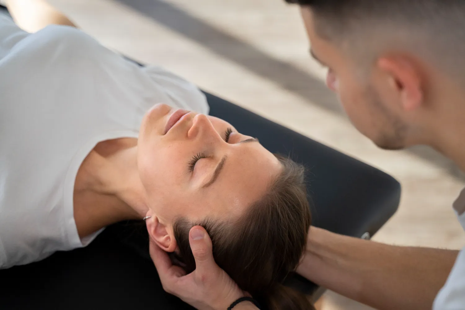 Therapist holding and supporting a woman's head during a treatment on a black surface.