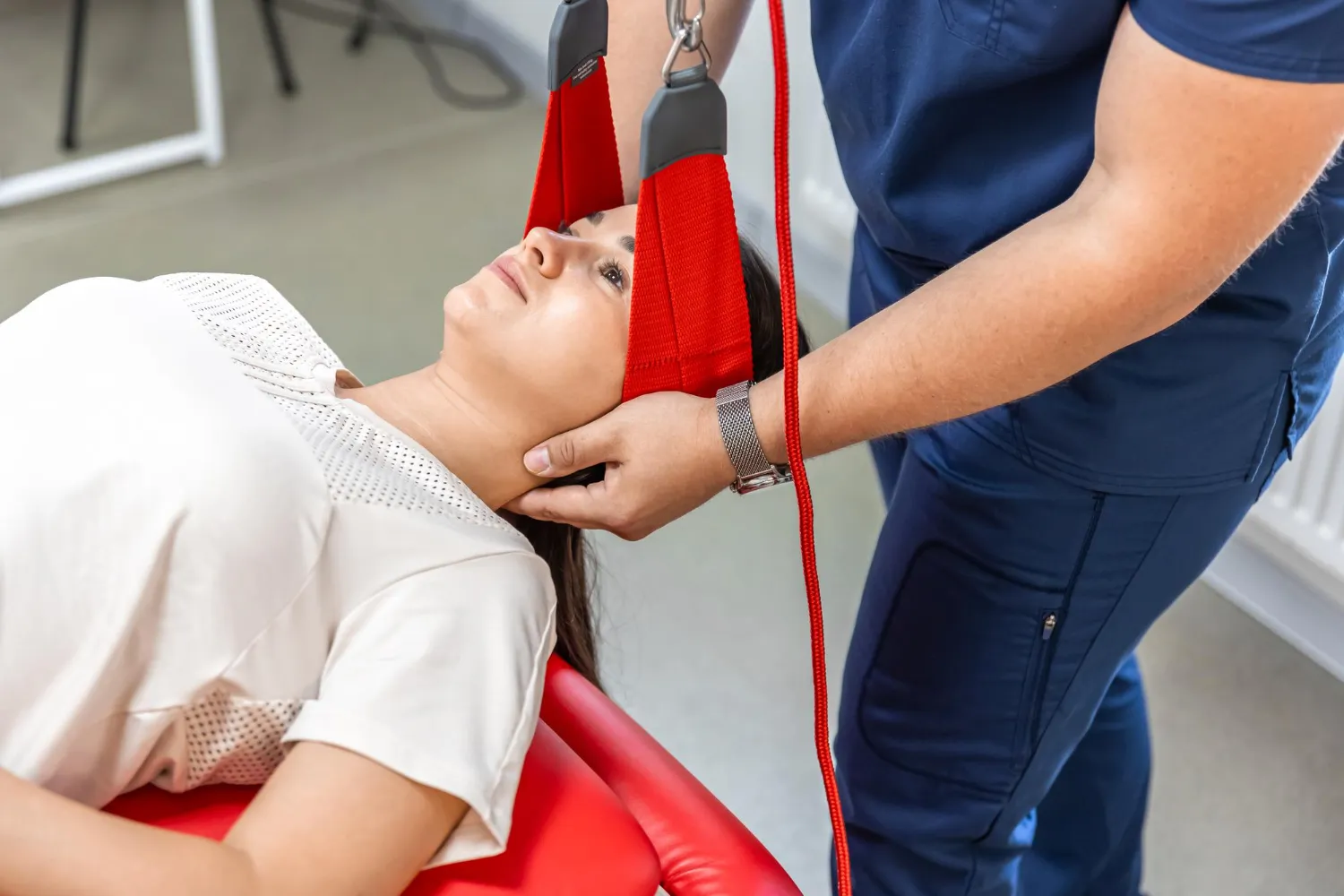 Therapist adjusting red neck traction device on a woman lying on a red treatment table.