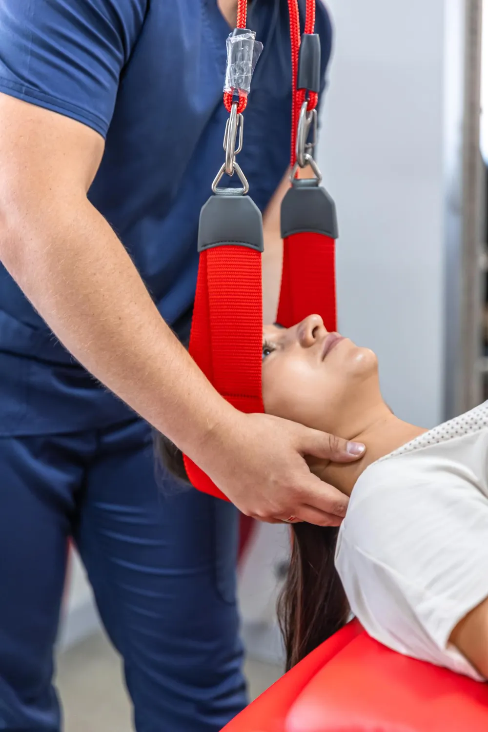Therapist supports patient's neck with red strap sling during cervical traction therapy session.