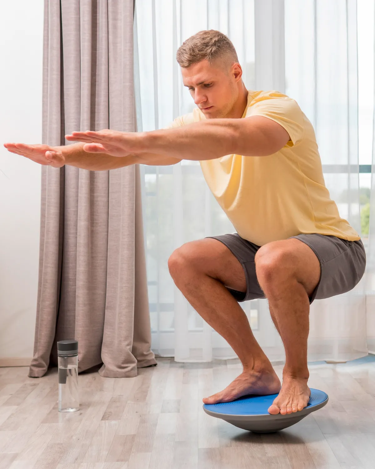 Man balancing barefoot on a blue balance trainer indoors with arms extended forward.