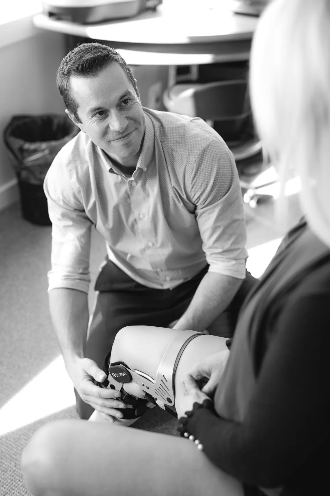 Man fitting a knee brace on a woman's leg in a clinical or office setting.