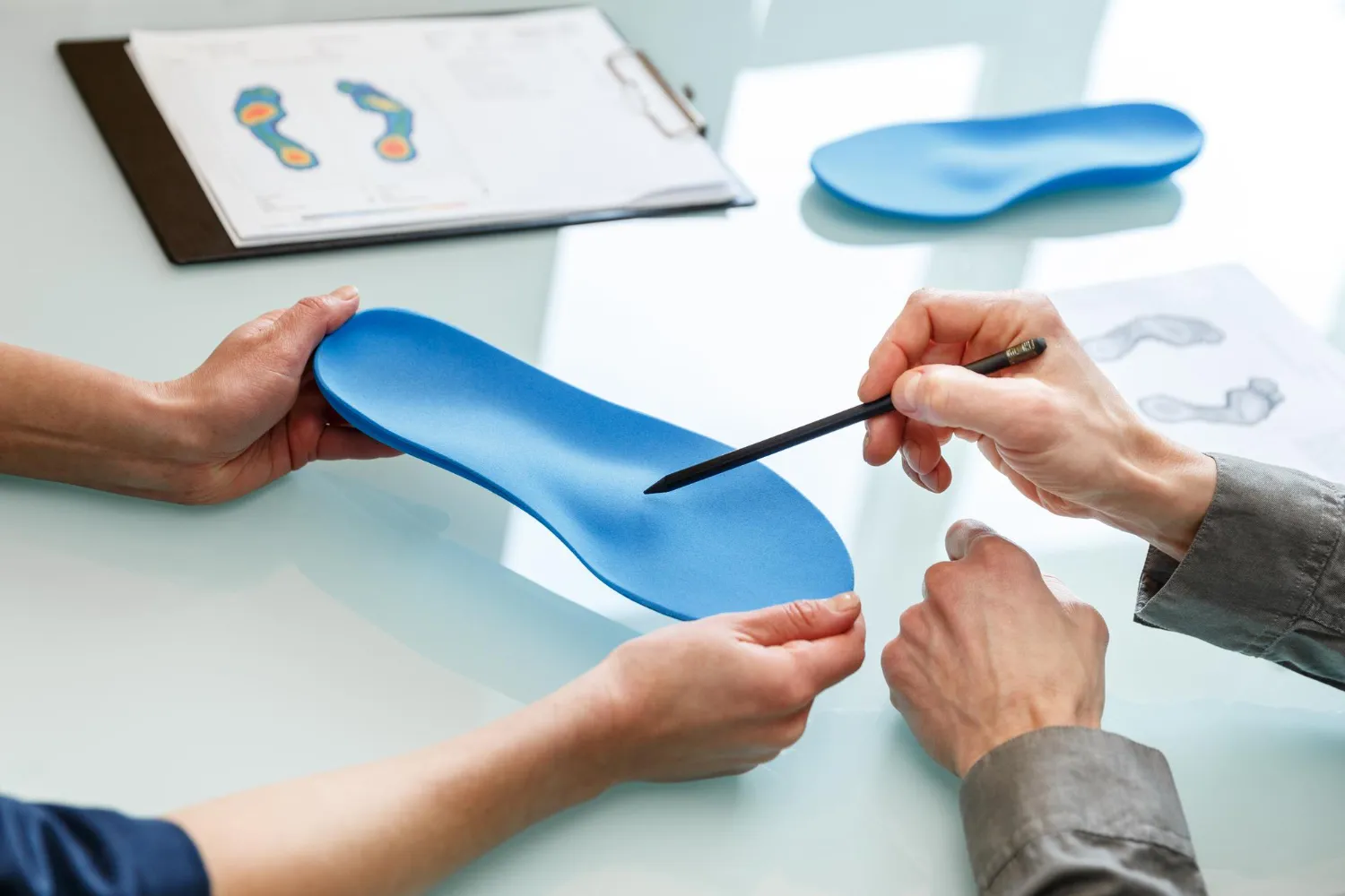 Two people examining a blue custom orthopedic insole with foot pressure charts on the table.