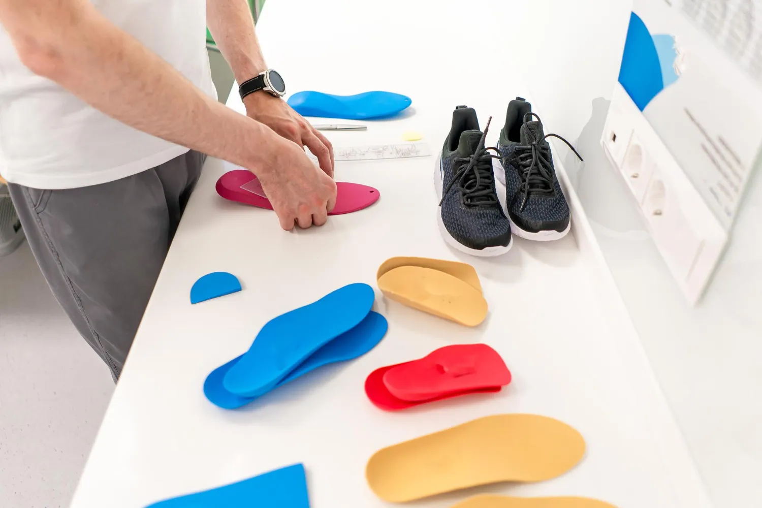 Person handling colorful custom orthotic insoles on a white surface next to black running shoes.