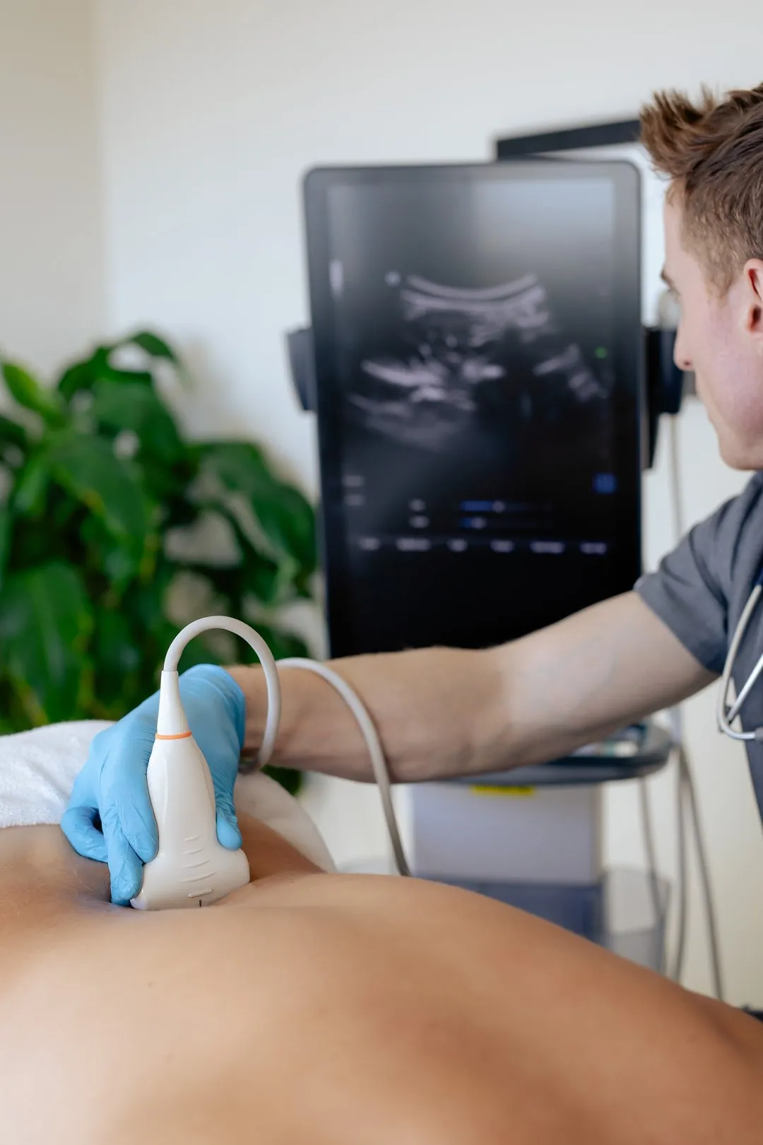 Doctor performing an abdominal ultrasound scan on a patient using a handheld transducer.