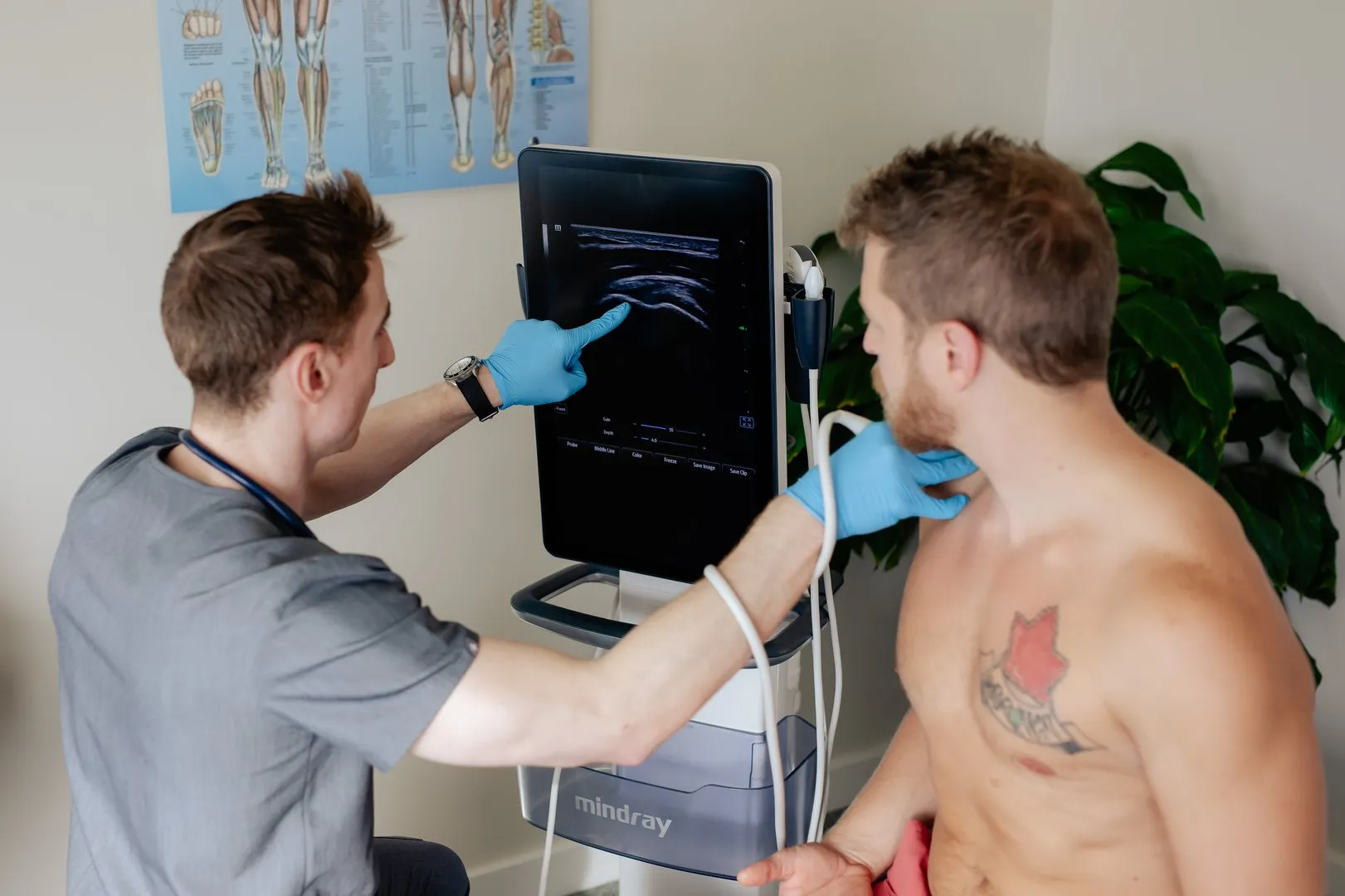 Medical professional in gloves performing a neck ultrasound on a shirtless man with a tattoo.
