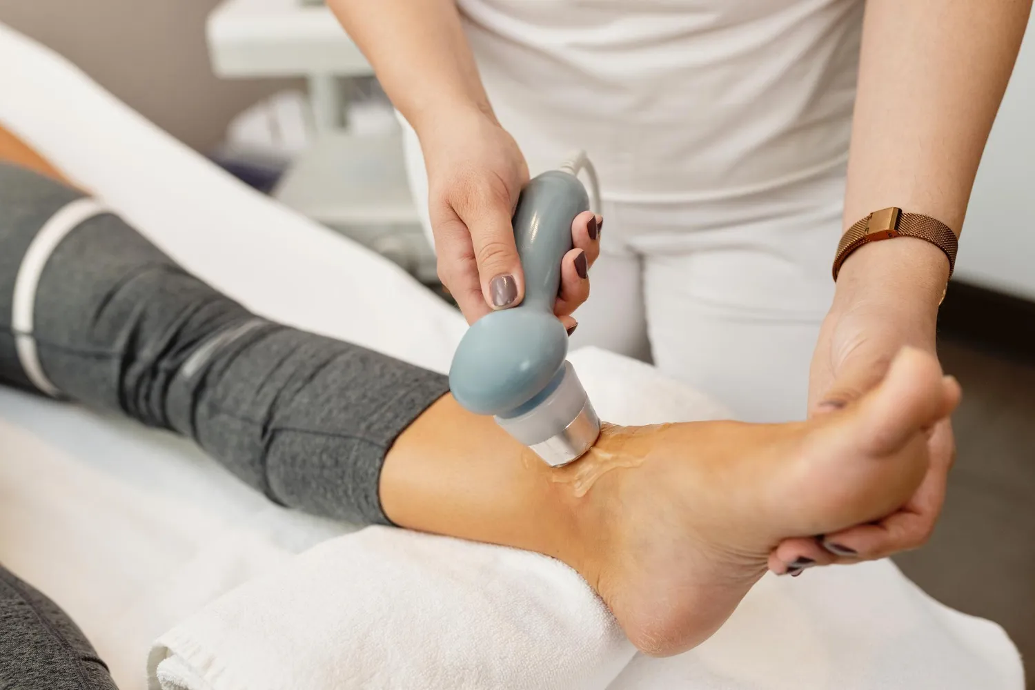 Therapist using ultrasound device on a patient's ankle for physical therapy treatment.