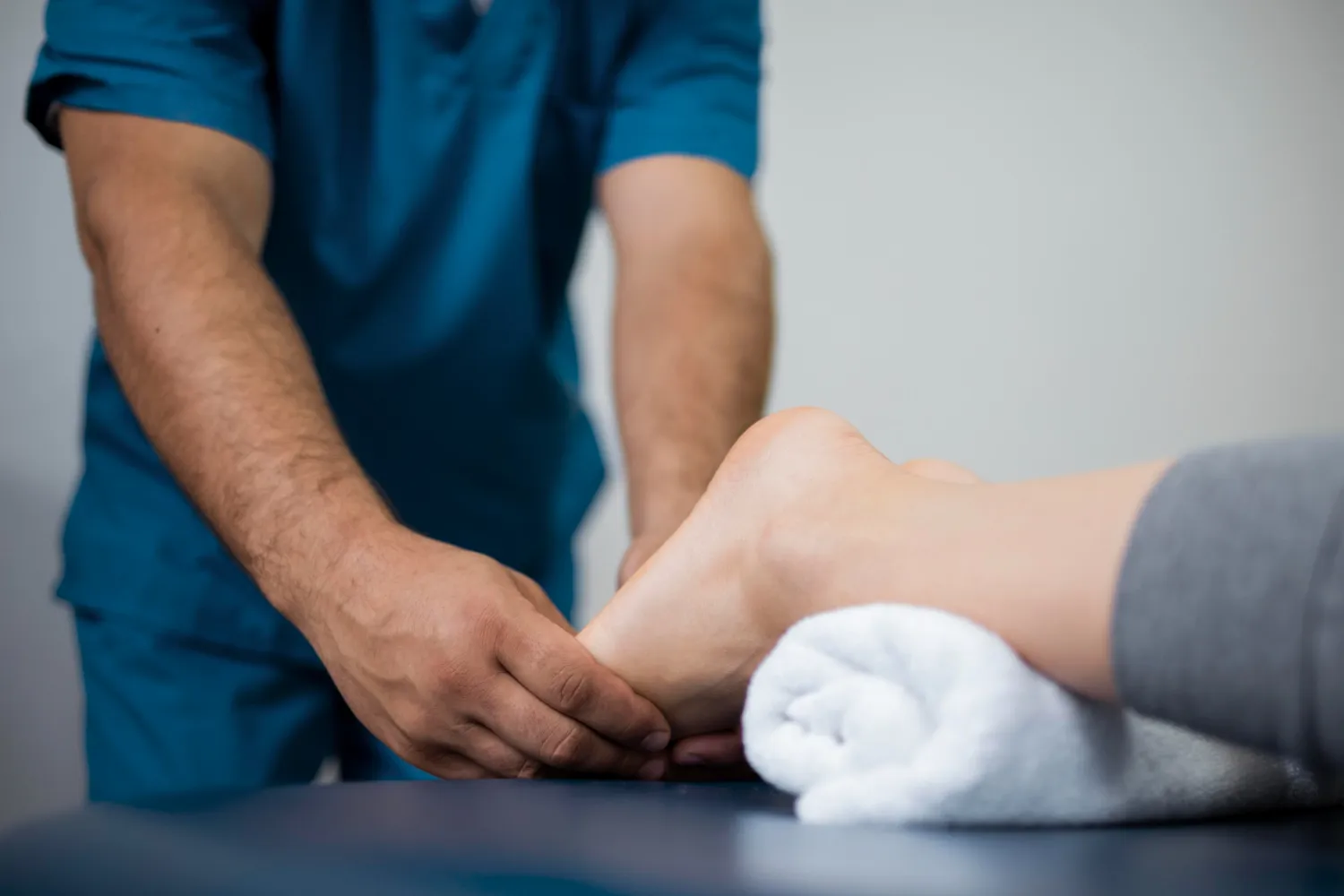 Therapist in blue scrubs holding and examining a patient's foot resting on a towel.