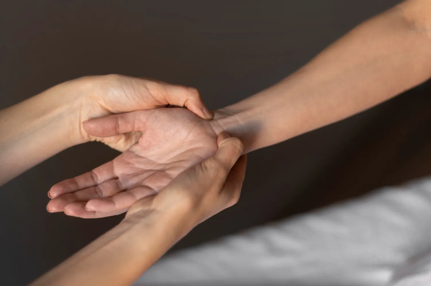 Person holding and checking another person's wrist pulse with both hands against a dark background.