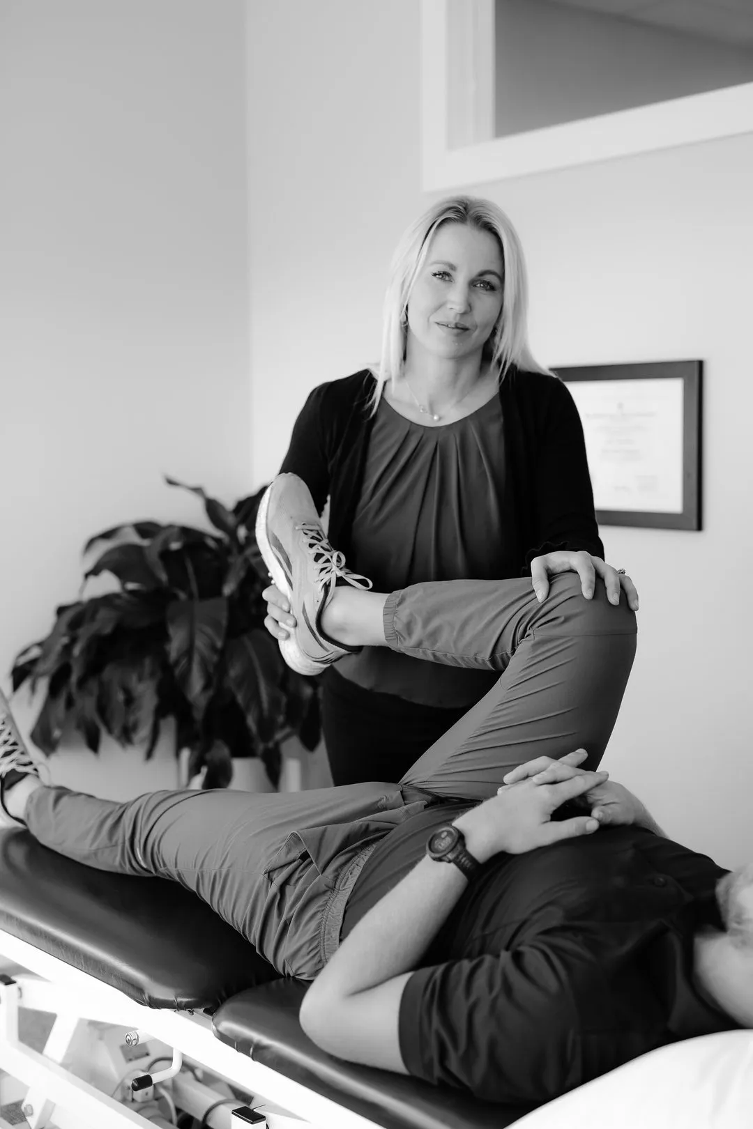 Female therapist stretching the bent leg of a male patient lying on a treatment table.