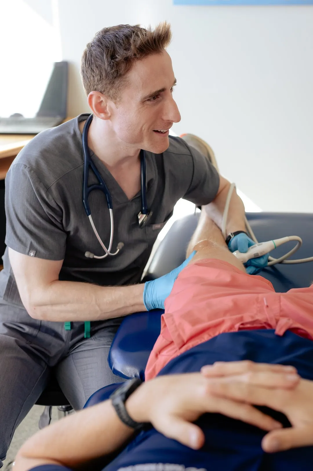 Medical professional using ultrasound device on patient's knee during examination in a clinic.