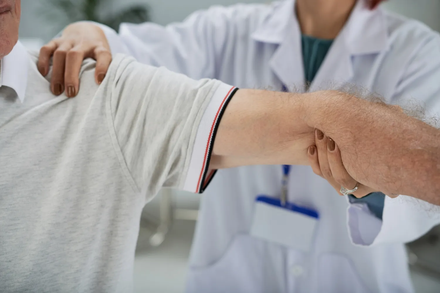 Healthcare professional in white coat examining an elderly man's arm by holding his elbow and shoulder.