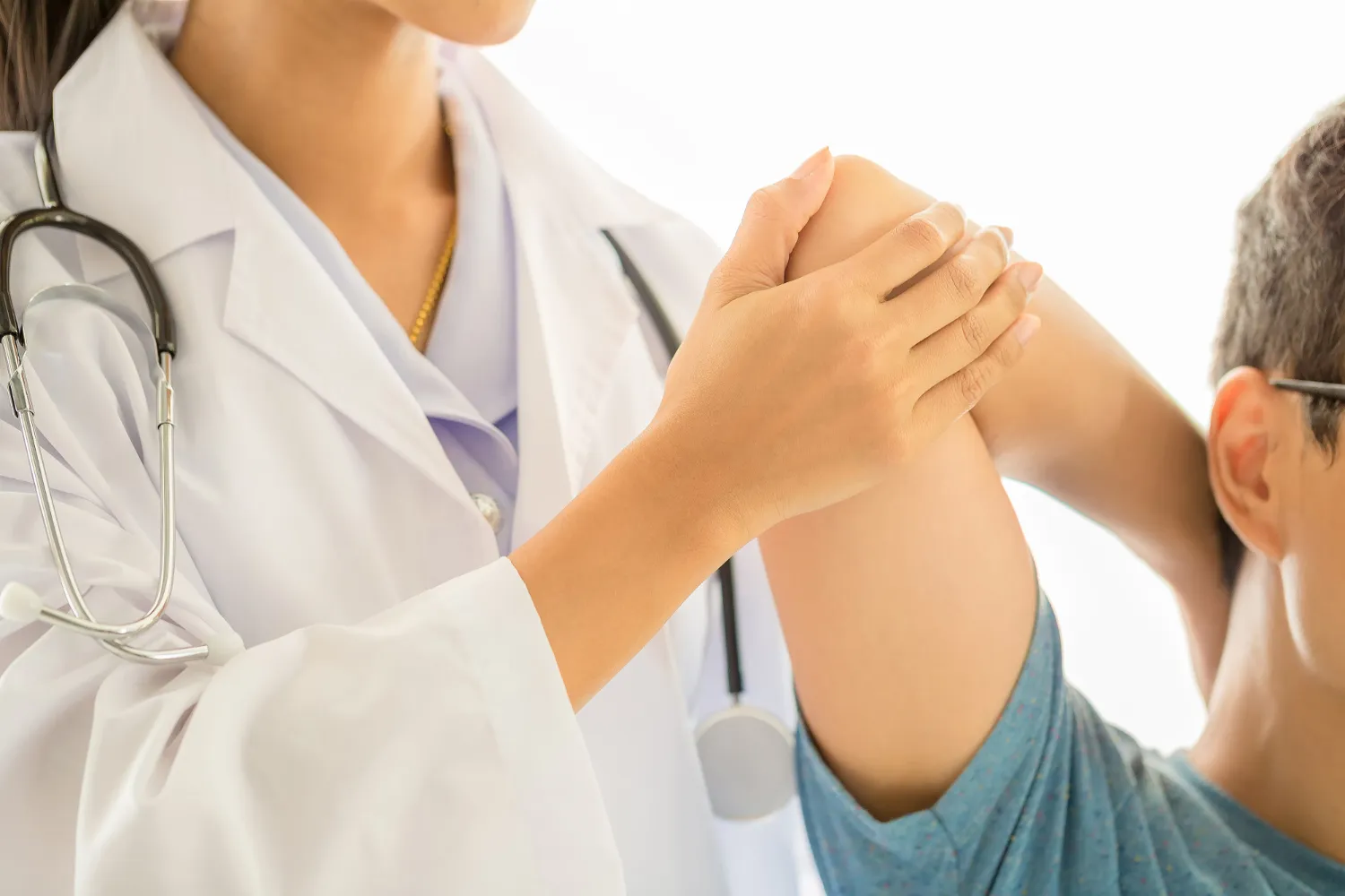 Doctor in white coat examining patient's bent elbow, checking joint movement and flexibility.