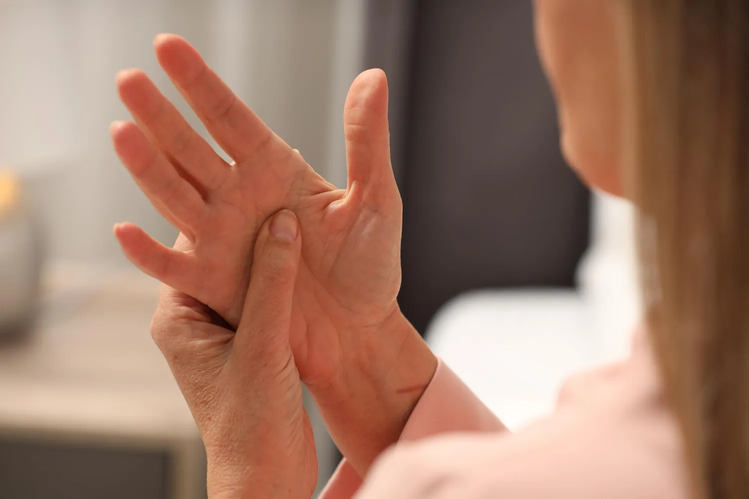 Person pressing thumb of left hand with fingers of right hand, suggesting hand pain or massage.