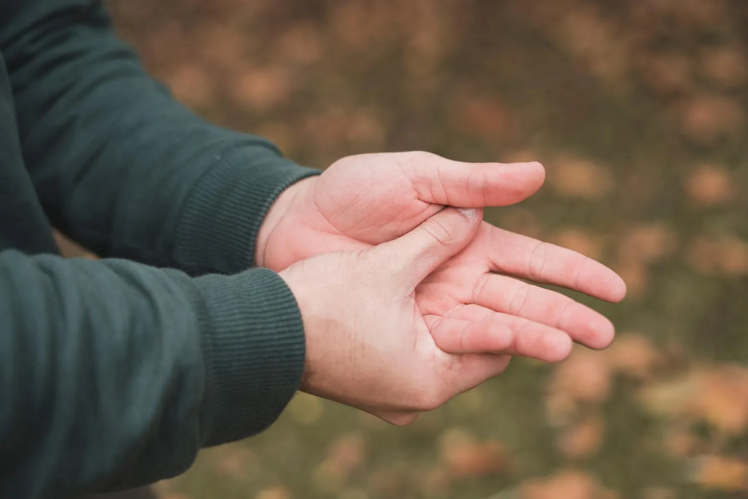 Person in a long-sleeve shirt holding and rubbing their left palm with their right hand.