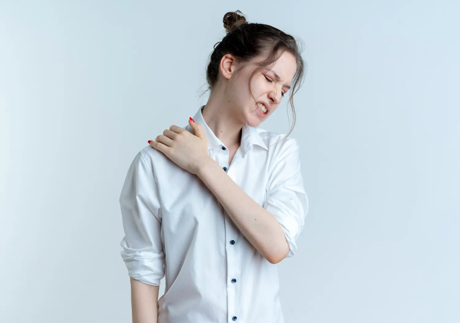 Woman in white shirt clutching her shoulder with a pained expression against a light blue background.
