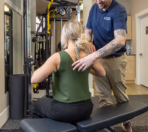 A trainer assists a seated woman using a resistance machine in a gym setting.