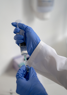 Healthcare professional wearing blue gloves preparing an injection with a syringe and medication vial.