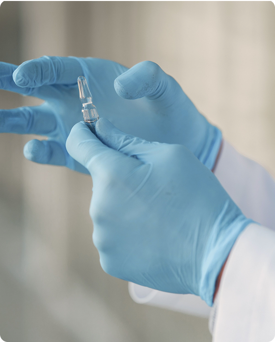 Healthcare professional wearing blue medical gloves holding a small glass medication ampoule.