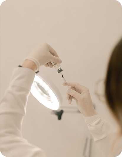 Healthcare professional preparing an injection by drawing medication from a vial into a syringe in a clinical setting.