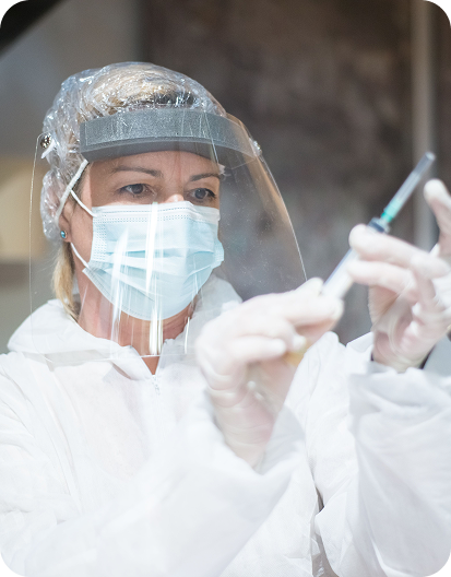 Healthcare professional wearing protective equipment preparing a syringe for an injection.