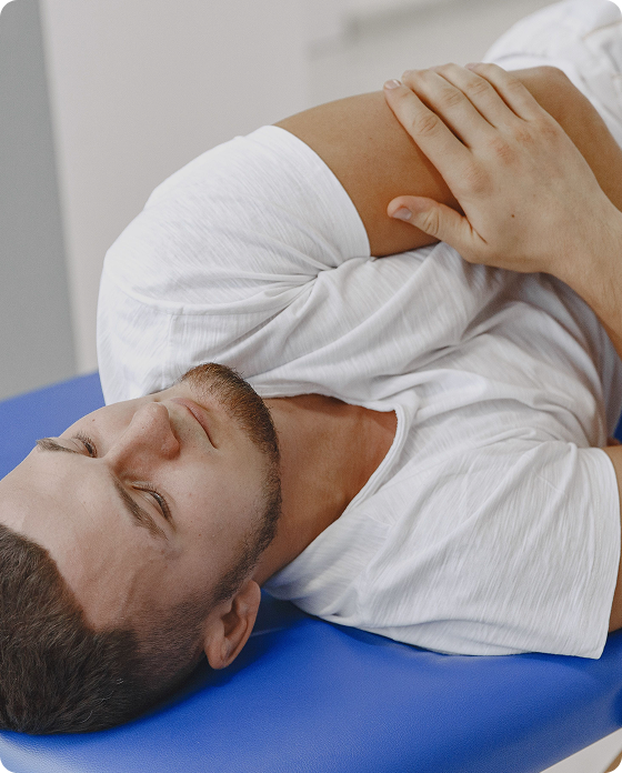 Patient lying on a treatment table while holding his shoulder, suggesting shoulder pain or discomfort.