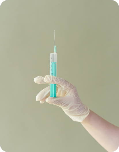 Healthcare professional wearing a glove holding a syringe filled with medication against a neutral background.