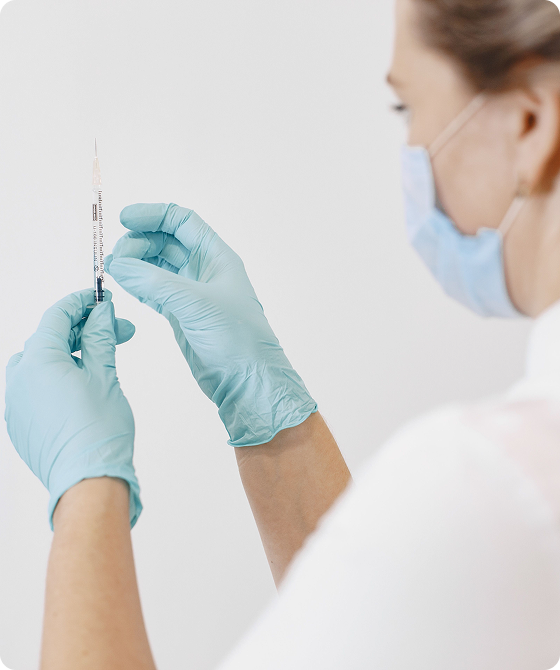 Healthcare professional wearing a face mask and blue gloves preparing a syringe for an injection.