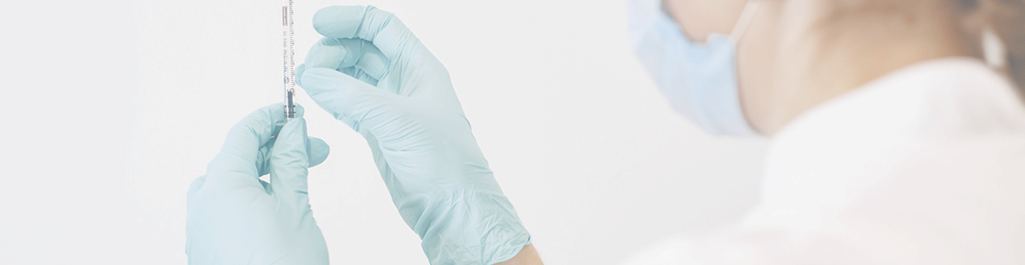 Healthcare professional wearing a face mask and blue gloves preparing a syringe for an injection.