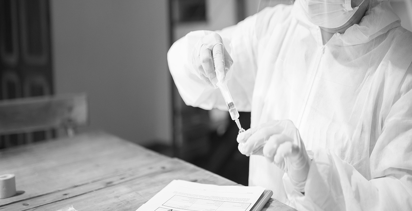 Healthcare professional in protective equipment preparing a syringe for injection therapy in a clinical setting.