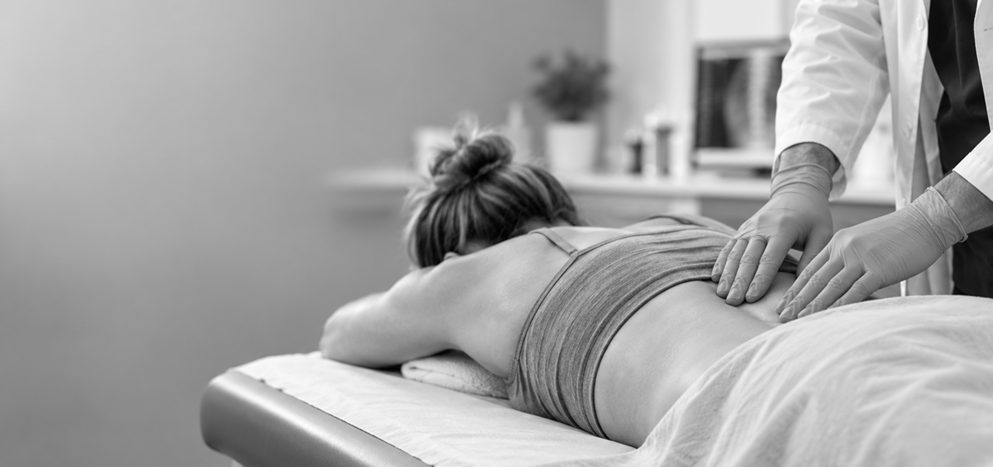 Healthcare professional performing a hands-on lower back examination on a patient lying on a treatment table.