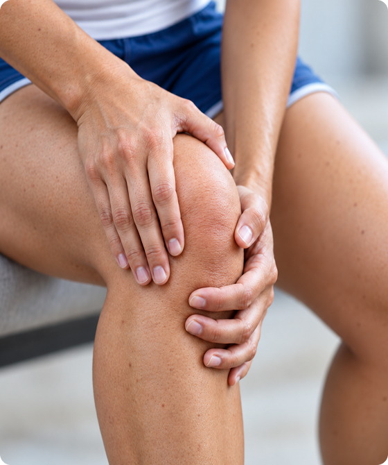Close-up of a woman holding her knee with both hands, indicating knee pain or discomfort.