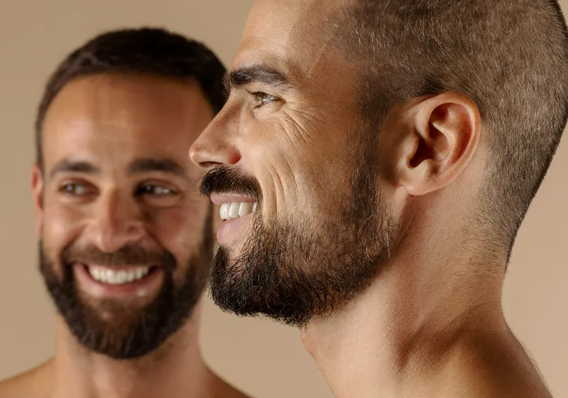 Two smiling men with beards, one in close profile and the other blurred in the background.