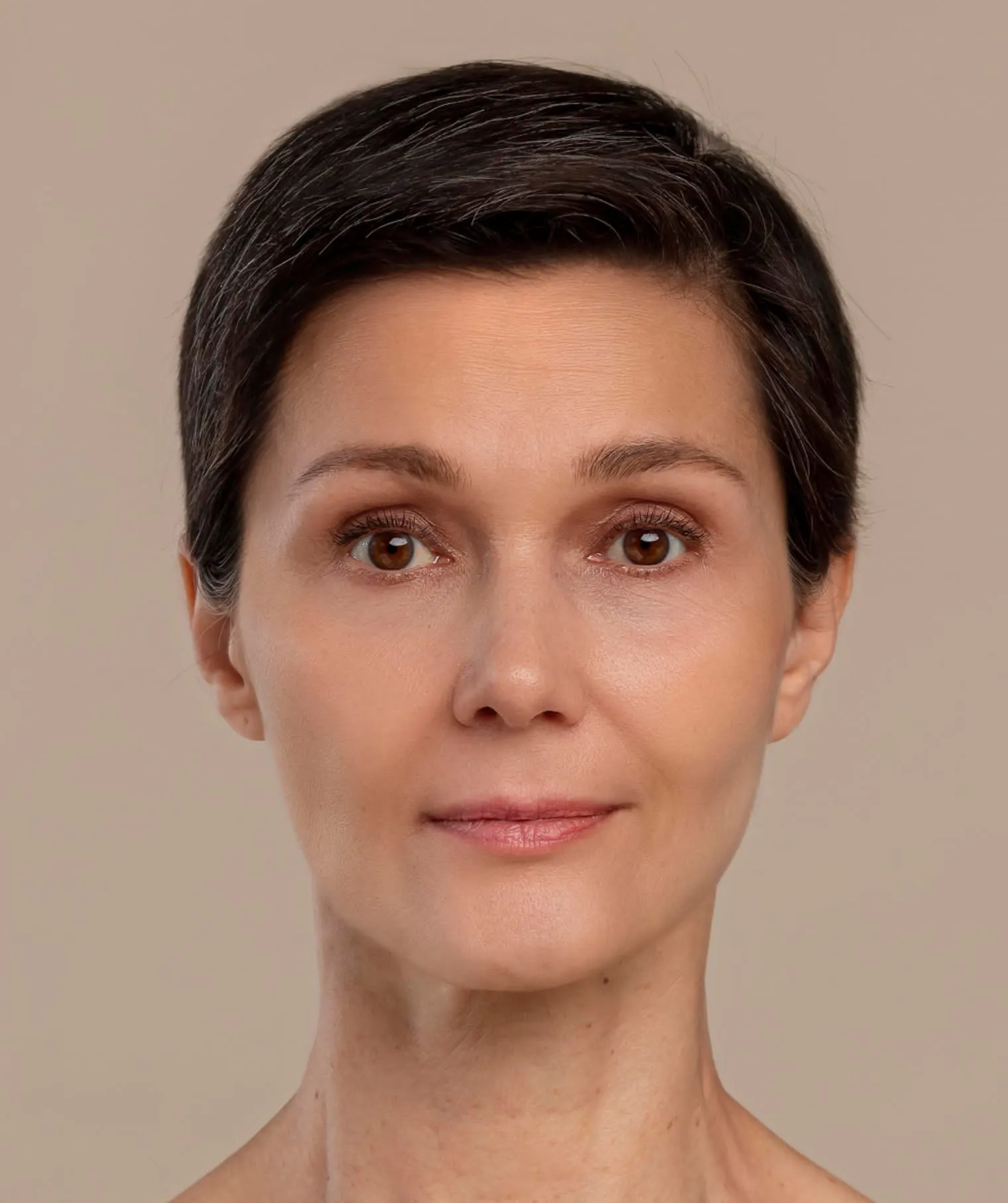 Close-up of a calm middle-aged woman with short dark hair and brown eyes against a beige background.