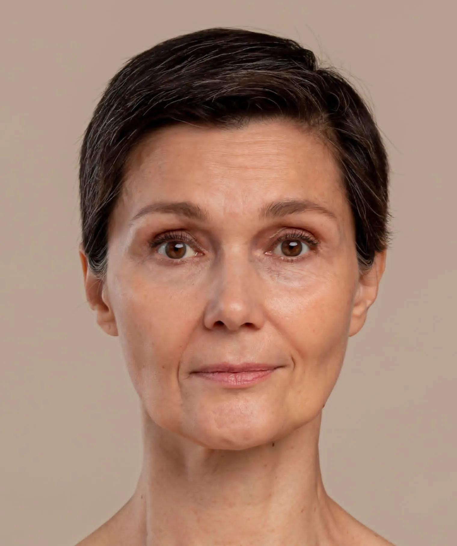Close-up portrait of a middle-aged woman with short dark hair and brown eyes against a beige background.