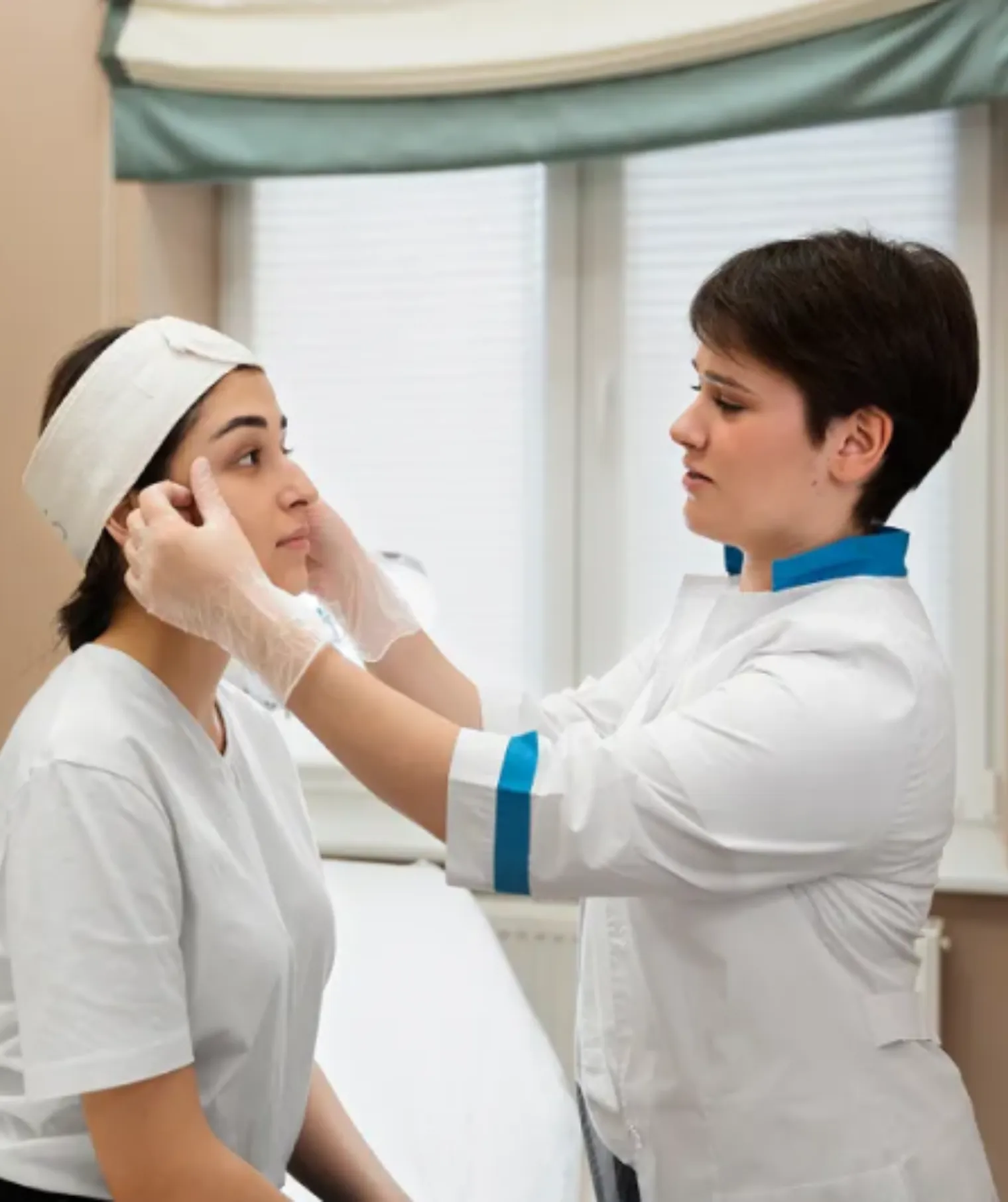 Medical professional wearing gloves examining a woman's face during a skin checkup in a clinic.