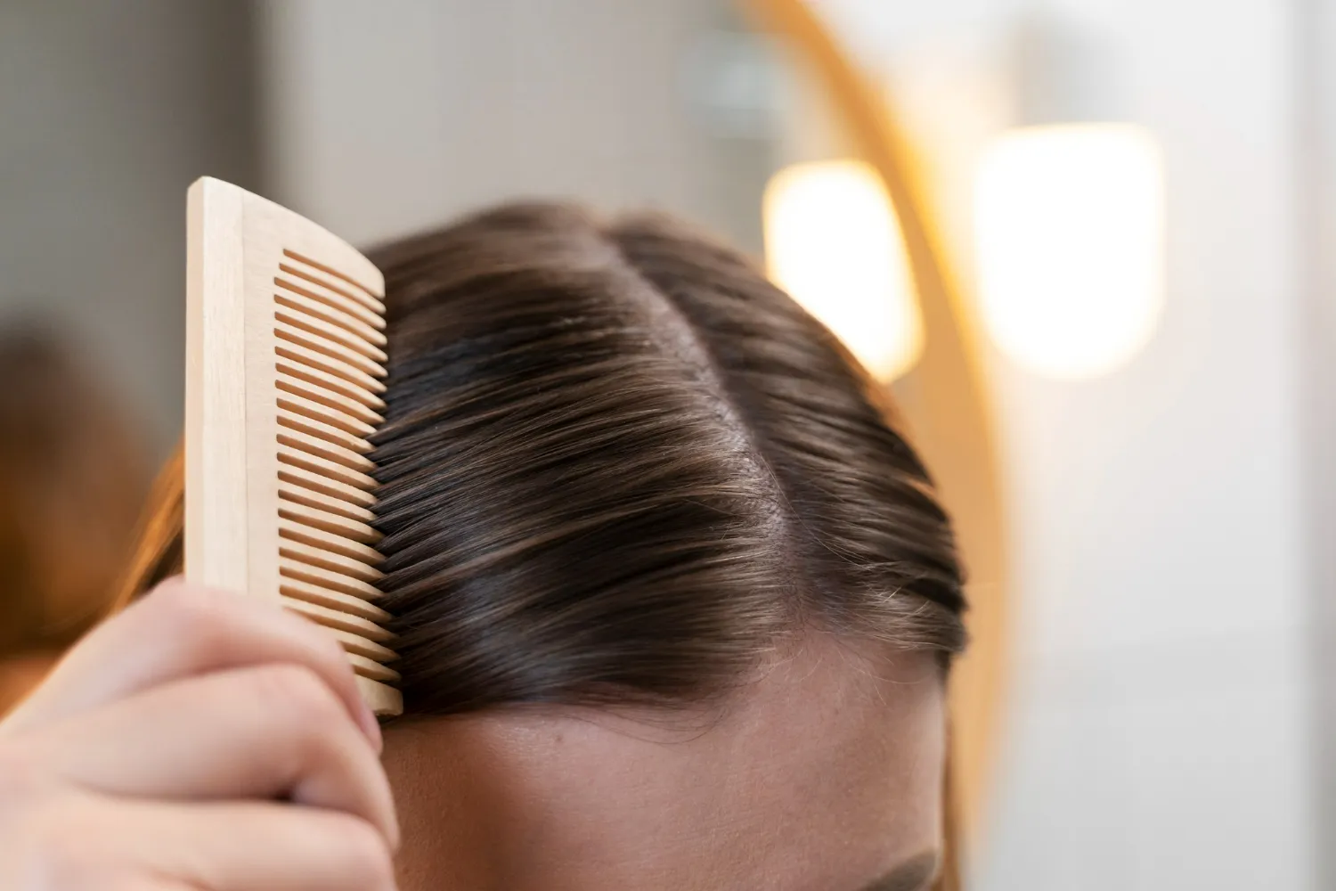 Close-up of person combing dark brown hair with a wooden comb, focusing on the scalp part.