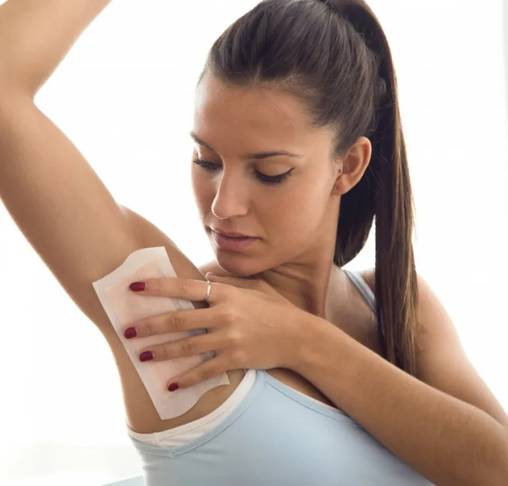 Woman using a wax strip on her underarm for hair removal.